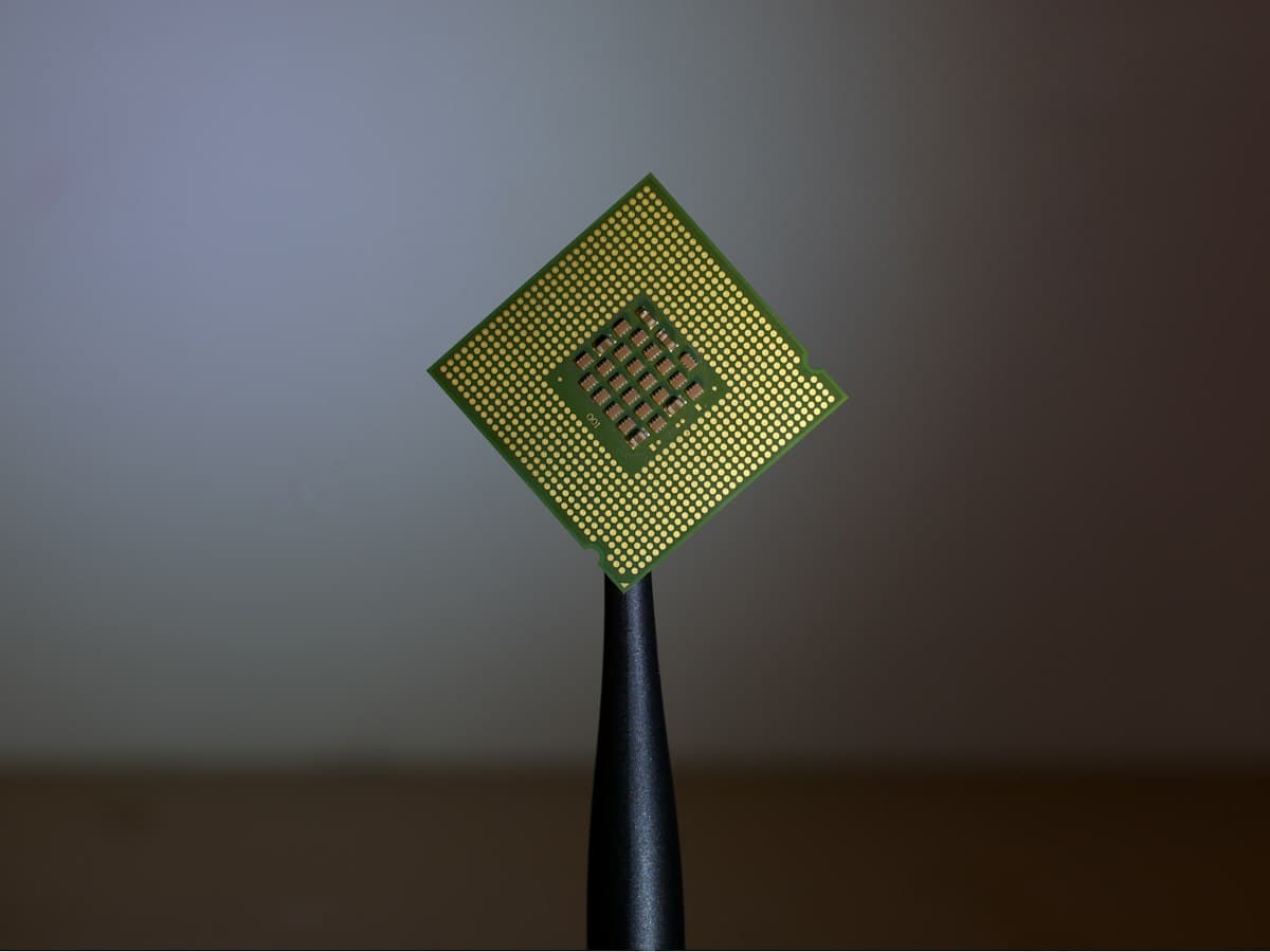 A processor held up by fine tweezers, its gold contact pins facing the camera.