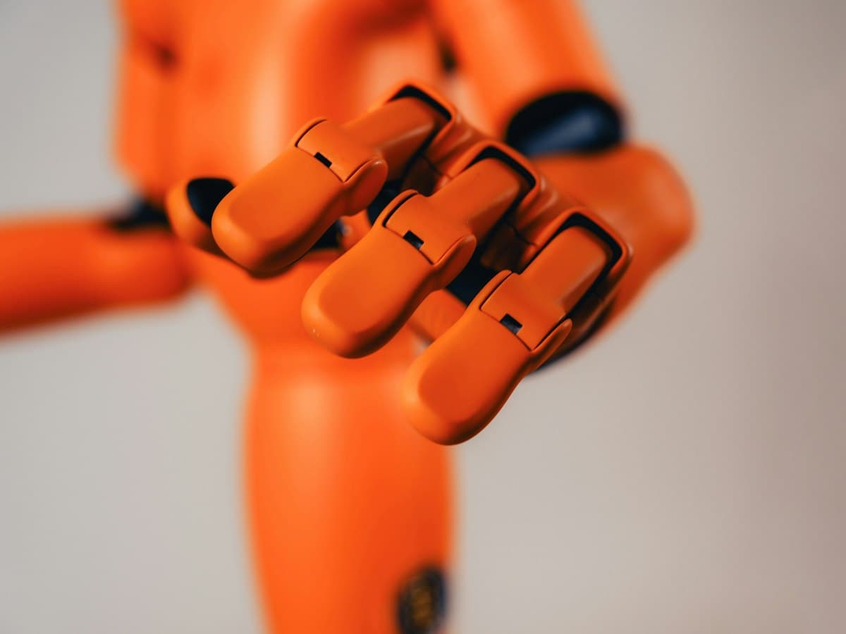 An articulated orange robotic hand reaching forward with its fingers slightly curled.
